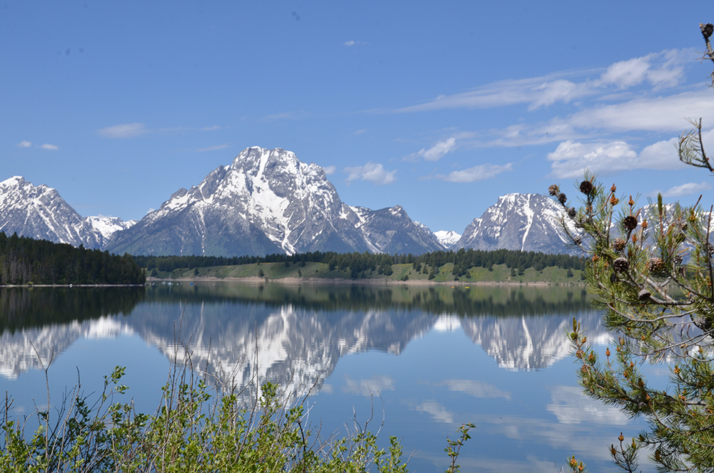 A massive snow-capped mountain range reflected in the shimmering waters of a large lake during the daytime.